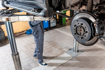 selective focus of assembled disc brakes near young mechanic examining raised car