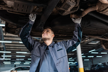 smiling mechanic inspecting bottom of raised car with wrench