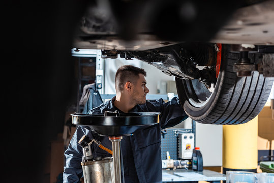 selective focus of mechanic standing under raised car near waste oil extractor