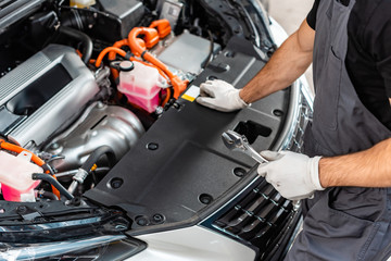 partial view of mechanic holding wrench while inspecting car engine compartment