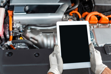 cropped view of mechanic holding digital tablet with blank screen near engine compartment