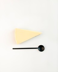 Piece of cheesecake wth a black spoon on minimal geometrical composition on white background