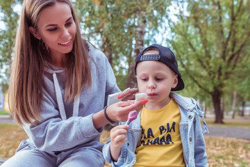 Happy family woman mom little boy son, eat ice cream, care for child, wipes face lips child with napkin, care and help. Autumn day on street in city park. Emotions joy of fun relaxation weekend.