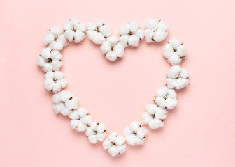 Heart shape made of cotton flowers on a pink background.