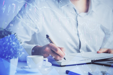 Double exposure of man's hands writing notes of stock market with forex chart.
