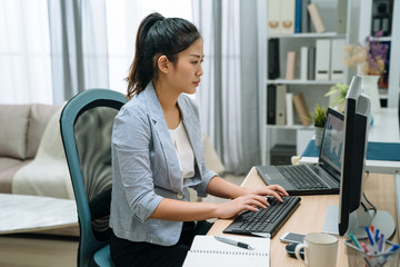 side view charming asian korean girl working at home on computer using her laptop also. female self...