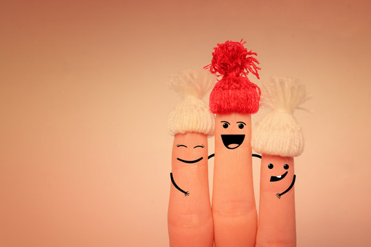 Fingers with painted faces in red knitted hats hug and smile on a pink background. Happy family concept. Copy space