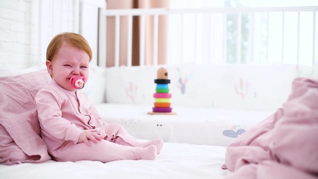 upset little baby girl crying on the bed, with dummy in mouth
