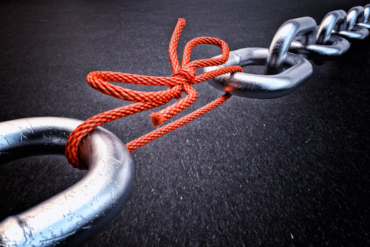 Weakest link, security break fix and strength concept, metallic chain connected by a red knotted rope on black background