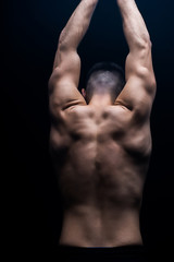 back view of sexy muscular bodybuilder with bare torso posing isolated on black