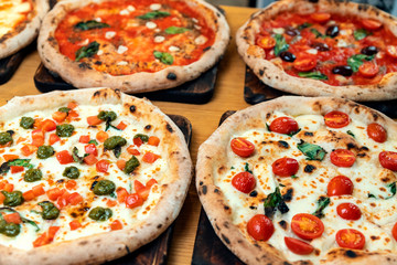 A lot of different freshly prepared pizza on a wooden table in an Italian restaurant
