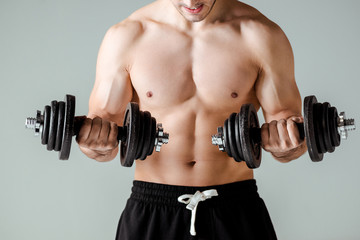 Fototapeta na wymiar partial view of sexy muscular bodybuilder with bare torso exercising with dumbbells isolated on grey