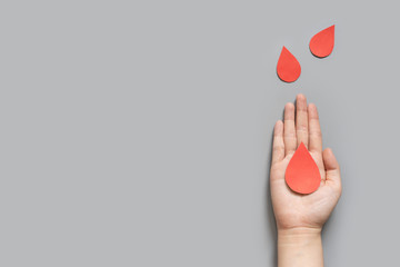 Blood donation - Human hand holding blood drop symbol on gray background with copy space. World blood donor day and save life concept. Flat lay. - obrazy, fototapety, plakaty