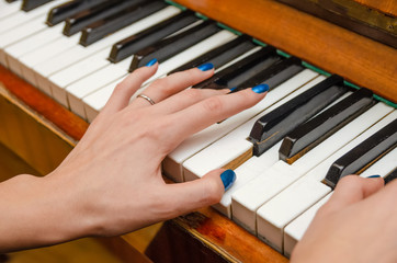 Fototapeta premium hands of a female pianist with blue nail Polish on the nails on the keys of a piano. girl playing the piano.