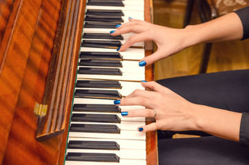 Fototapeta premium hands of a female pianist with blue nail Polish on the nails on the keys of a piano. girl playing the piano.