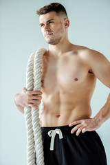 Obraz premium niski kąt widzenia sexy muskularny kulturysta z nagim torsem, pozowanie z liny bojowej na szarym tle