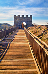 Beautiful view with wooden bridge leading to a stone gate of an ancient fortress