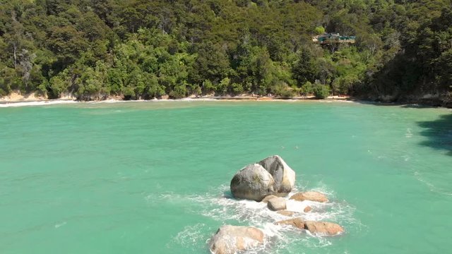 Aerial clip of a beach in the Abel Tasman National Park, New Zealand, and a strange rock that looks like a split apple in the middle of the sea.