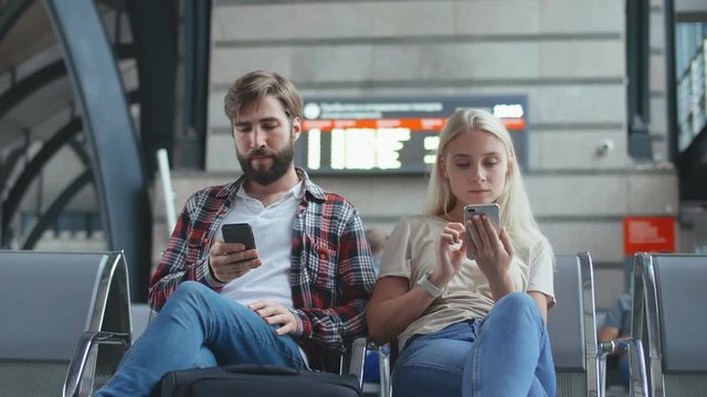 Photo of man and woman with phones in their hands sitting in waiting room at airport