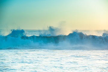 California beach, USA. Pale pastel teal aqua blue greens of water and skies. Abstract sunset seascape background. Crashing Pacific Ocean sea waves in beautiful soft yellow sunsetting light