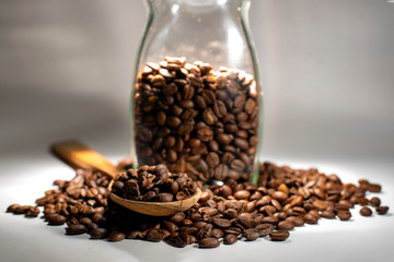 Coffee beans in a wooden spoon with glass jar on dark background