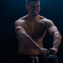 Fototapeta na wymiar tense sexy muscular bodybuilder with bare torso excising with kettlebell on black background