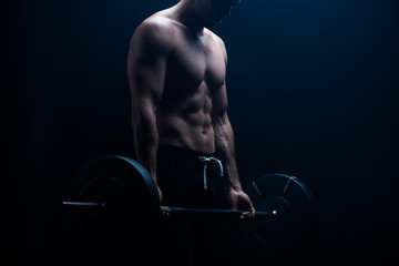 cropped view of muscular bodybuilder with bare torso excising with barbell on black background