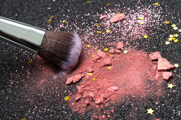 Closeup of crushed pink blusher and fluffy brush, decorative stars for makeup on the black surface
