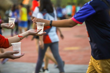 Hand of a volunteer giving a cup of water at a refreshment point in a marathon race to runners.