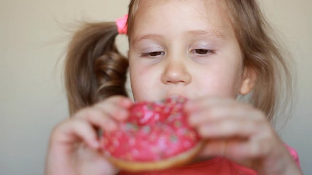 Child mouth bites rose donut. Closeup baby girl eating doughnut with glase. Delicious, sweet, sweettooth.