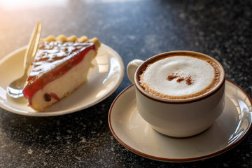 Cup of foamy cappuccino coffee served with raspberry pie. Soft and warm morning light added.