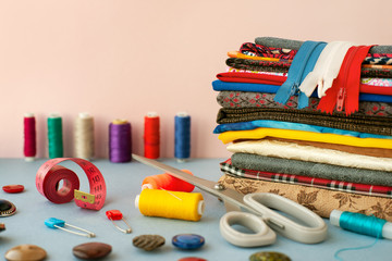 Cloth, scissors, threads and needles as accessories for sewing. A stack of fabrics, threads,...