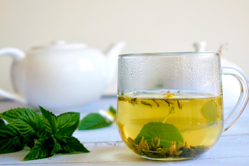 A Cup of green tea on a white background with mint leaves and a teapot
