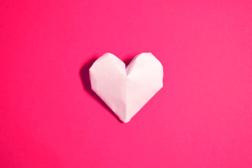 The Background Of Valentine's Day. One heart made of origami paper, in the center on a pink background. The Concept Of Valentine's Day. Flat lay. Top view, copy space.