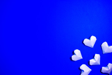 The Background Of Valentine's Day. White origami paper hearts on a blue background. The Concept Of Valentine's Day. Flat lay. Top view, copy space.