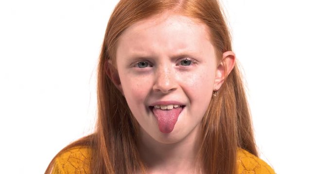 Funny little girl looking in camera showing tongue. Young model with beautiful foxy hair with freckles making grimaces and having fun