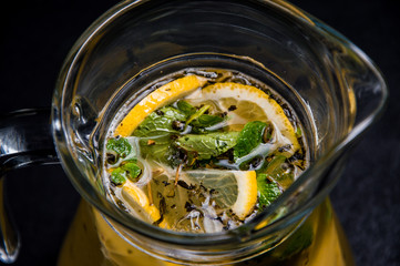 natural lemonade with lemon, mint and ice . soft drink in a jug on a black, isolated background . sparkling water with syrup. close-up of fruit.