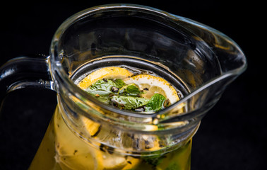 natural lemonade with lemon, mint and ice . soft drink in a jug on a black, isolated background . sparkling water with syrup. close-up of fruit.