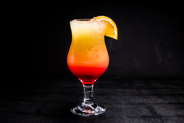 Tequila sunrise cocktail with ice and a slice of citrus. a glass with an alcoholic drink on a...