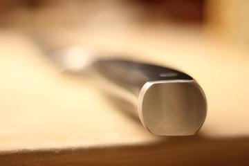 Macro of a steel knife on a wooden desk.
