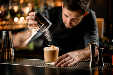 Male bartender serving the creamy color alcoholic drink decorated with a candy sprinkling on it with sugar powder