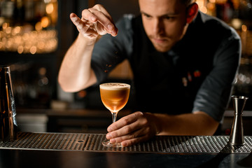 Male bartender serving the brown alcoholic drink sprinkling on it with spices