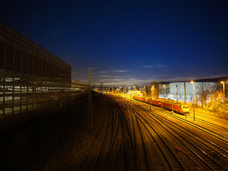 Railway engines on an illuminated freight yard, with multiple railway tracks, in an industrial area, under a starry sky