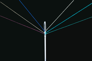 negative image of multiple colored threads passing through the eye of a needle