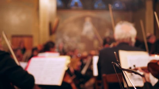 Orchestra musicians turning sheet music at classic concert, soft focus.
