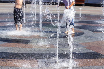 Children splashing in the city fountain. Hot summer day.
