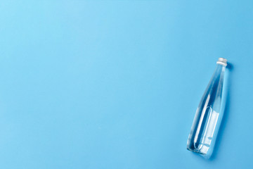 Glass bottle with clear water on a blue background. Concept of health and beauty, water balance, thirst, heat, summer. Flat lay, top view