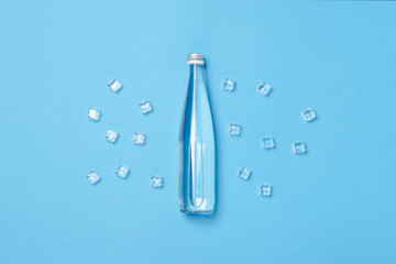 Glass bottle with clear water on a blue background with Ice cubes. Concept of health and beauty,...