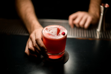 Fototapeta na wymiar Professional bartender serving the red color alcoholic cocktail drink decorated with a little rose bud