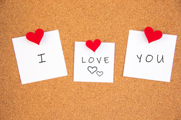 I love you handwriting lettering with heart on 3 white papers pinned with 2 big red heart pegs and one small red heart pegs on cork board